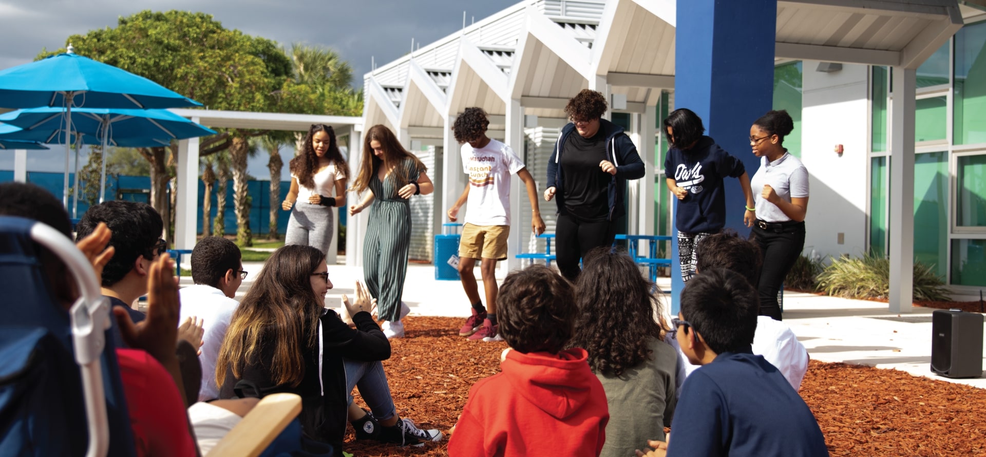FAU High students gathered outside under blue umbrellas, participating in a school activity